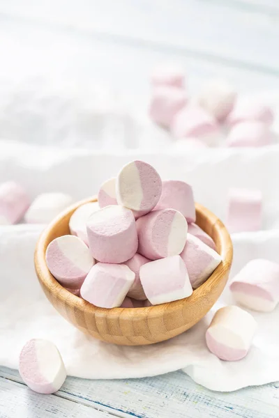 Portrait of a wooden bowl full of pink and white marshmallows with some scattered around on a white table cloth — Stock Photo, Image
