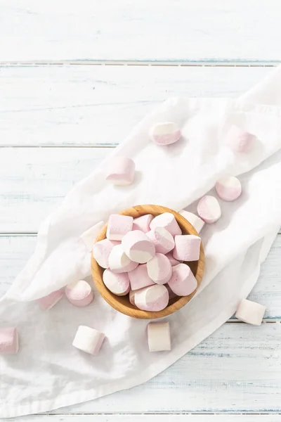 Top portrait view of a wooden bowl full of pink and white marshmallows with some scattered around on a white table cloth — Stock Photo, Image