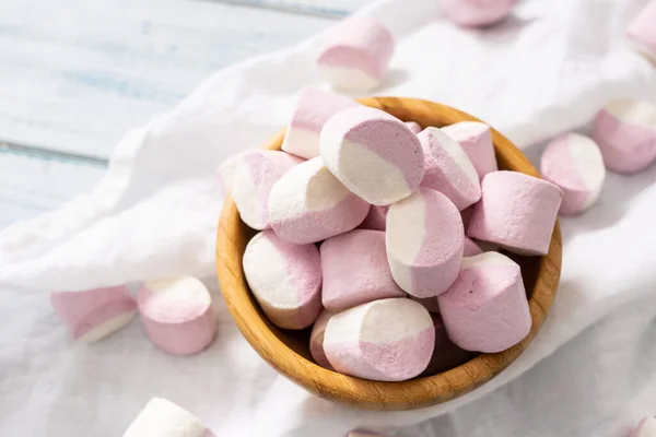 Wooden bowl full of pink and white marshmallows with some scattered around on a white table cloth — Stock Photo, Image