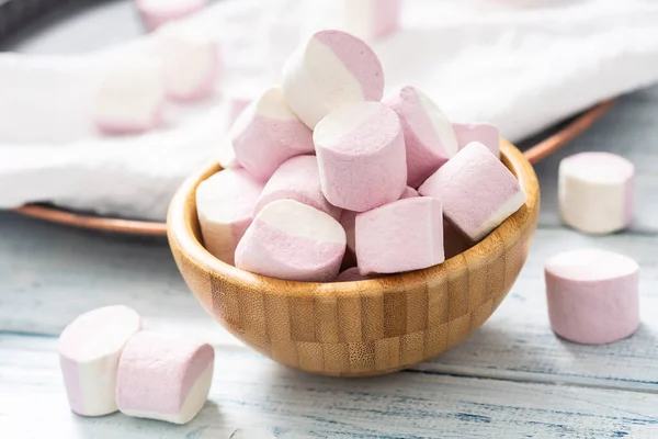 Close up of a wooden bowl full of pink and white marshmallows with some scattered around on a white table cloth, dark tray and white wooden table — Stock Photo, Image