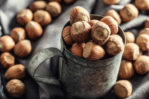 Närbild av en vintage metallic mugg full av hasselnötter med mer nötter på en textilduk runt den — Stockfoto