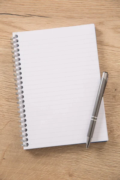 White lined notepad with a metal ring wire binding and a silver pen opened on a wooden surface — Stock Photo, Image