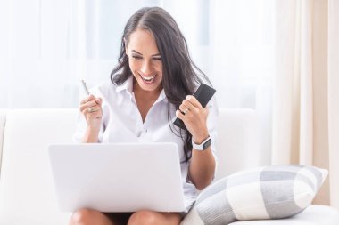 Mutlu evli bir kadın, oturma odasındaki koltukta otururken bilgisayarından okuduğu haberleri kutluyor. Elinde cep telefonu ve kalemle yumruklarını sallıyor..