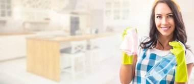 Önlüklü gülümseyen güzel bir kadının pankart görüntüsü. Elinde deterjan ve arka planda mutfak olan plastik eldivenlerle elindeki bez parçasını temizliyor..