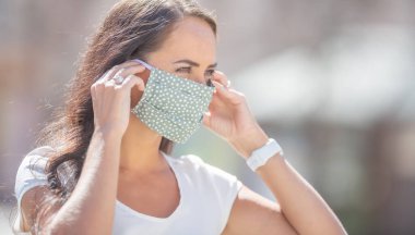 Güzel kız, güneşli bir günde puantiyeli maskesini kulaklarına geçirir..