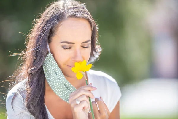 美しい女性は 自然の中で晴れた日に目を閉じて 彼女の顔のマスクの半分と花の香りを楽しんでいます — ストック写真