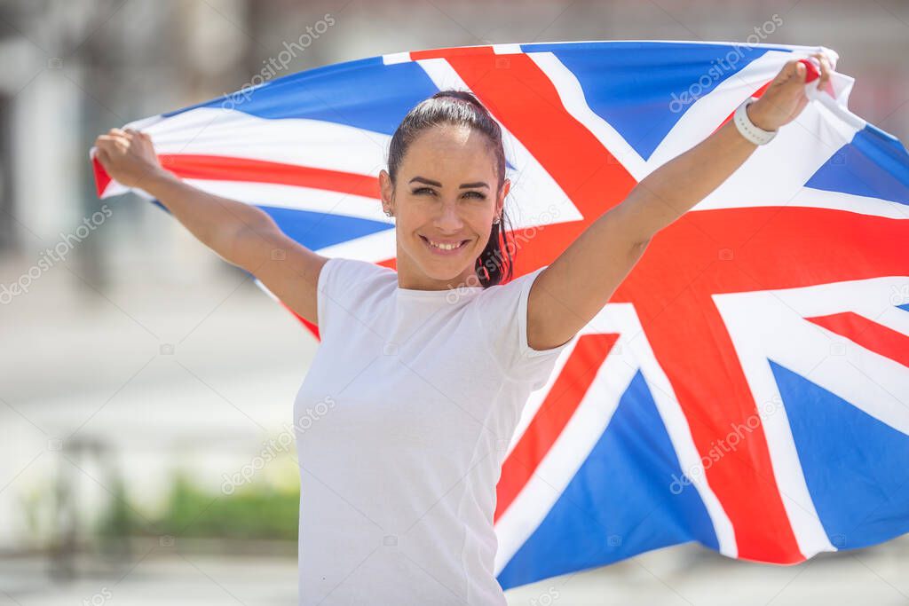 Pretty girl ina white t-shirt holds a flag of Great Britain behind her, smiling at the camera.