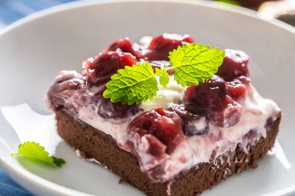 Detail of a piece of brownie with a cream, cherries and fresh mint leaves on a plate — Stock Photo, Image