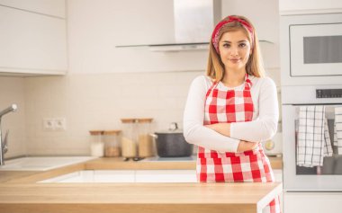 Genç bayan kendine güvenerek mutfakta duruyor. Önlük giyiyor.. 