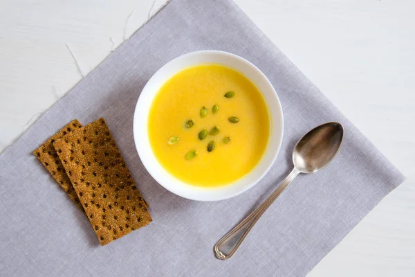 Soup of pumpkin and sunflower seeds in a white plate with a silver spoon and bread on a linen napkin. The concept of healthy eating, weight loss, diet, health care