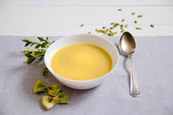 Soupe à la crème de citrouille aux graines de citrouille dans des assiettes blanches avec une cuillère en argent sur une serviette en lin . — Photo