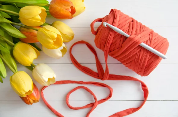 Rotolo di filato di cotone e un uncinetto con un bouquet di tulipani arancioni e gialli su sfondo bianco di legno. Il concetto di uncinetto, hobby, cucito, autorealizzazione, creatività — Foto Stock