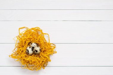 Beyaz ahşap zemin üzerinde dekoratif yuvadaki bıldırcın yumurtası. Üstten Görünüm. Kopya alanı