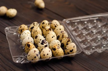 Koyu ahşap arka plan üzerinde plastik bir kapta bıldırcın yumurtası. Yakın çekim