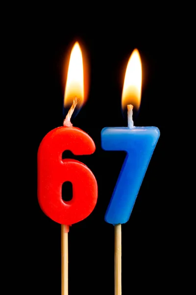 67, 67 の形のキャンドルを燃焼 (数値、日付) に黒の背景で隔離のケーキ。誕生日、記念日、重要な日付、休日、テーブルセッティングを祝っての概念 — ストック写真