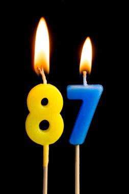 87 seksen yedi şeklinde mum yakma (sayılar, tarihler) siyah arka plan üzerine izole kek için. Kutluyor doğum günü, yıldönümü, önemli bir tarih, tatil, Tablo ayarı kavramı