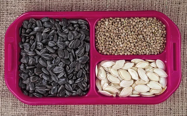 Sunflower seeds, pumpkins and hemp in the red cells. Seeds of various oilseeds against the background of coarse tissue.