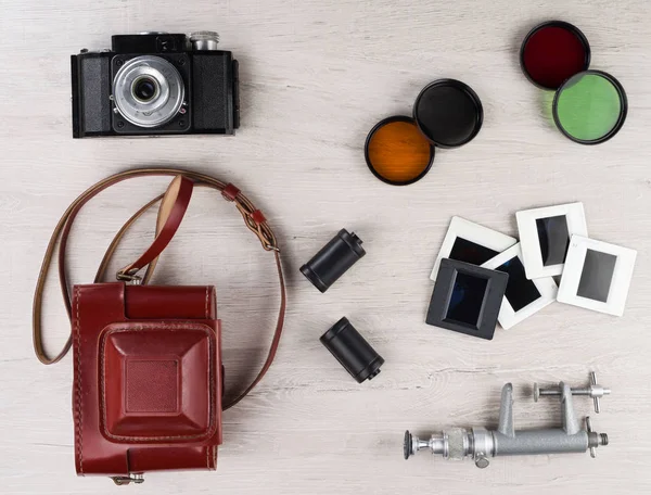 Vintage camera with a red leather case, cassettes, color filters, slides and a mini stand on a surface.