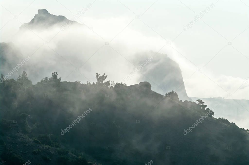 Mountain ridge against the backdrop of a mountain peak in the fog and sky.