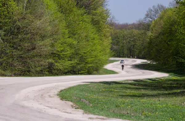 A winding road in the forest. A car and a bicyclist on a winding road in a forest. Selective focus.