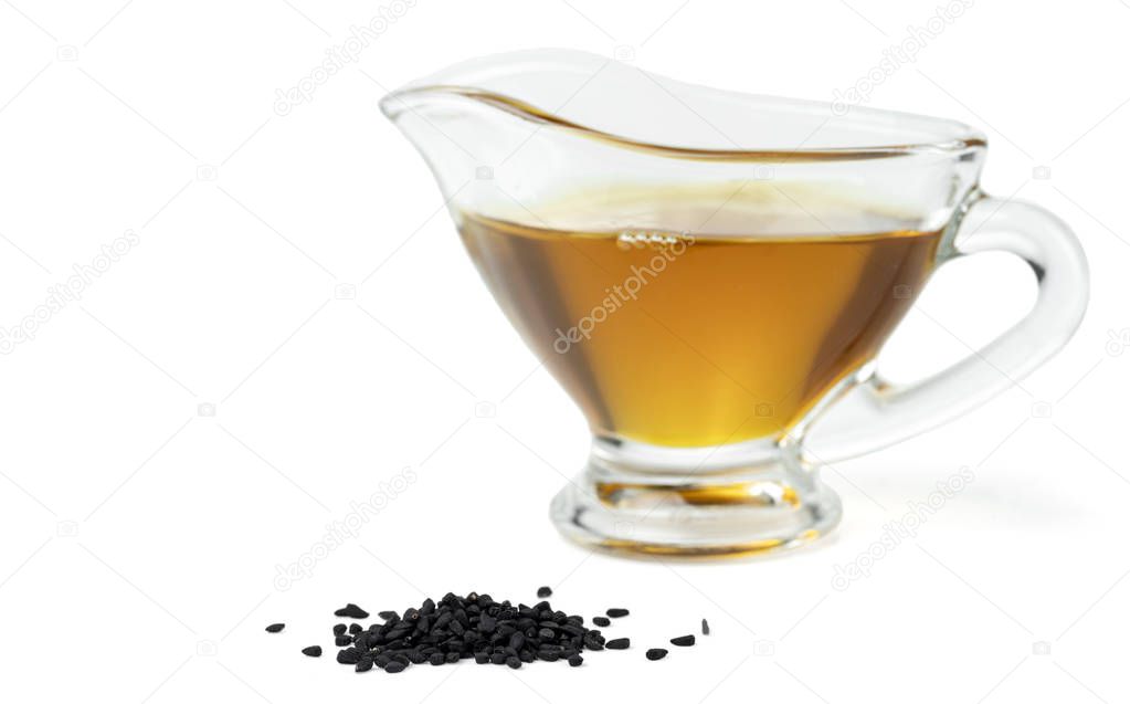 A handful of black cumin seeds and black seed oil in a glass gravy boat. Isolated on white background.