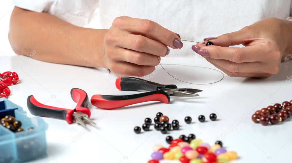 Making bracelet of colorful beads. Female hands with a tool on a white background. Selective focus