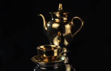 Siyah bir arka planda, bulanık bir çaydanlık ile izole edilmiş bir fincan altın sarısı çay..