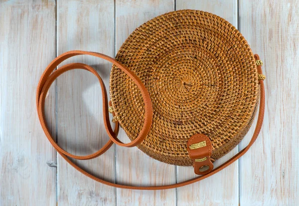 A ladies handbag braided with brown strap on a wooden rough painted background.