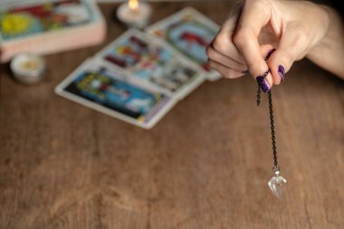 Arm of dowser with hand-held pendulum on the background of tarot cards. Selective focus. clipart