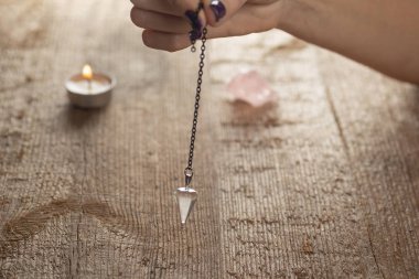 Pendulum on a chain with a natural crystal on a background of wood texture with burning candles. Selective focus. clipart