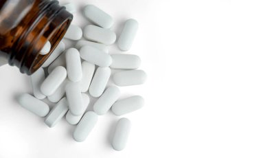 Beyaz arka planda siyah cam bir şişenin yanında beyaz oval haplar..  