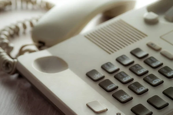 Desk phone on the desk with the handset off. Selective focus.