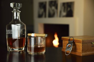 şöminede ateş tarafından ısıtılan çevre zarflama. bir bardak içki, bir şişe ve bir puro ön planda