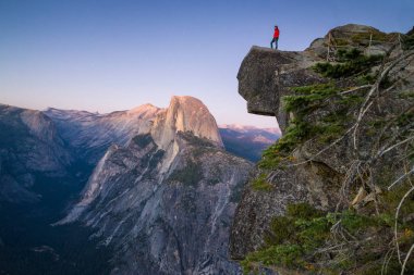 Korkusuz bir uzun yürüyüşe çıkan kimse güzel yazı günbatımı alacakaranlıkta, Yosemite Milli Parkı, Kaliforniya, ABD manzarayı buzul noktası overlook adlı ünlü Half Dome doğru çıkıntılı bir kaya üzerinde duruyor