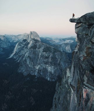Korkusuz bir uzun yürüyüşe çıkan kimse güzel yazı günbatımı alacakaranlıkta, Yosemite Milli Parkı, Kaliforniya, ABD manzarayı buzul noktası overlook adlı ünlü Half Dome doğru çıkıntılı bir kaya üzerinde duruyor