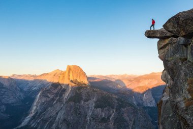 Korkusuz bir yürüyüşçü güzel akşam alacakaranlık, Yosemite Ulusal Parkı, Kaliforniya, ABD'de güzel akşam alacakaranlık bakan Glacier Point ünlü Yarım Kubbe doğru manzarasının keyfini sarkan bir kaya üzerinde duruyor