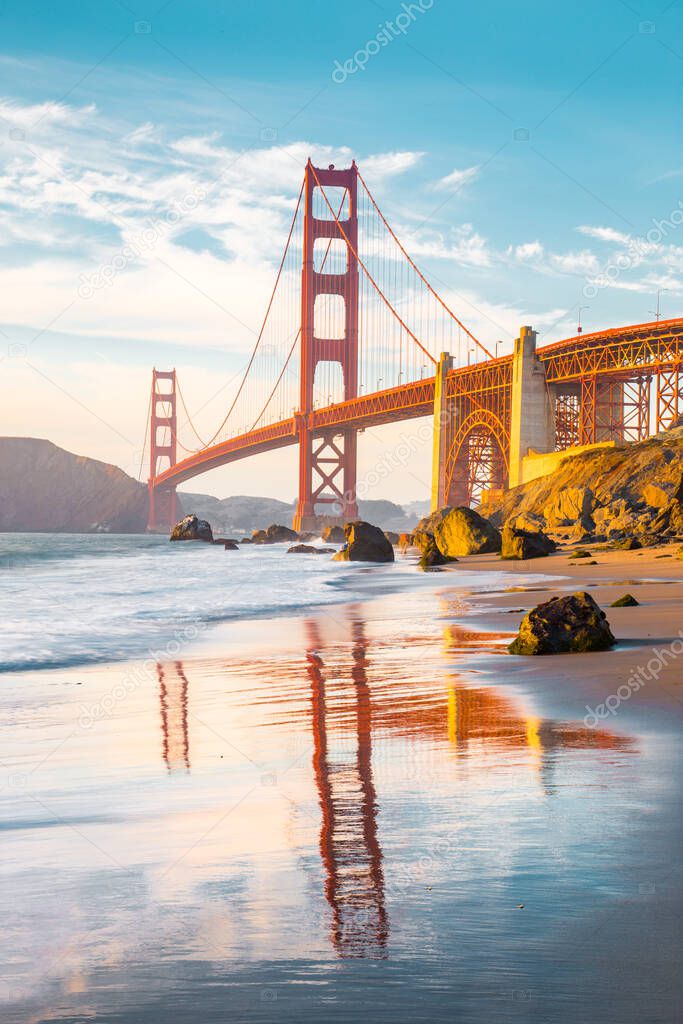 Classic panoramic view of famous Golden Gate Bridge seen from scenic Baker Beach in beautiful golden evening light on a sunny day with blue sky and clouds in summer, San Francisco, California, USA