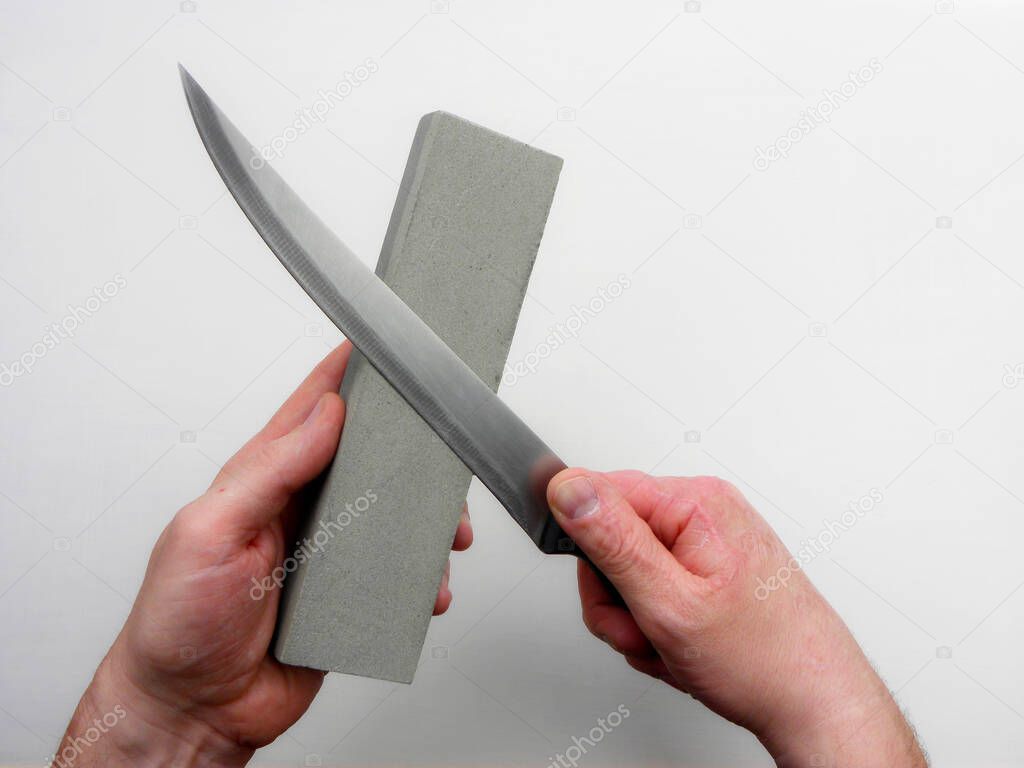 Sharpening a knife by sharpening a stone on a white background. Men's hands use a whetstone to sharpen a knife blade.                               