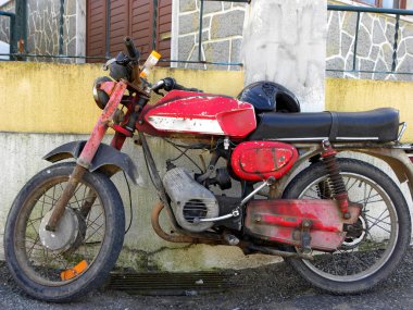    Eski binaların yakınına park edilmiş krom motorlu eski bir kırmızı. Paslı eski kırmızı motosiklet                                               