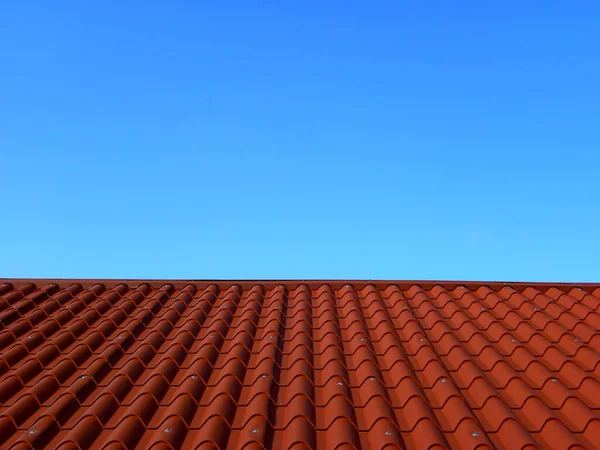 Red tile roof under blue sky. The photo is divided in half. One part is a roof made of clay tiles and the other is a pure blue sky.