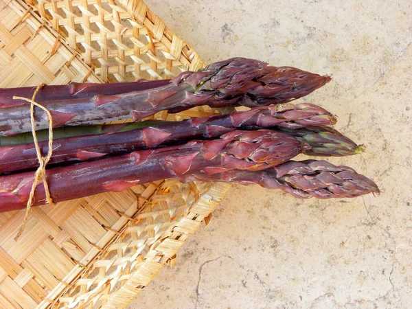 Bej renkli mermer bir yüzey üzerinde sepette duran bir buket taze Mor Kuşkonmaz..