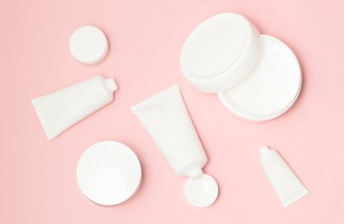 Beyaz kozmetik tüpler ve pembe bir arka plan üzerinde krem kapları Üstten Görünüm