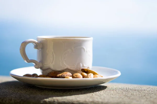 Cup of coffee with decorative nuts, with lake in soft focus — Stock Photo, Image