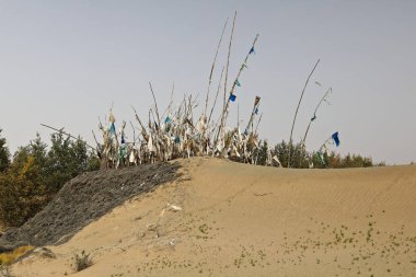 Taklamakan Çölü 'nün kıyısındaki rüzgârlı kum tepecikleri arasında, mistik İmam Asım' ın mazar-masolyum sahasındaki gömülü tepenin üzerine adak bayrakları. Hotan Şehir-Xinjiang Uygur Özerk Bölgesi - Çin.