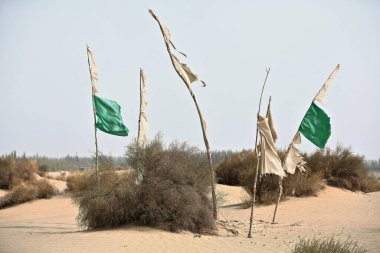 Mezar höyüklerindeki adak bayrakları, Taklamakan Çölü 'nün kıyısındaki rüzgârlı kum tepecikleri arasında sufi mistik İmam Asım' ın mazar-masolyum alanına işaret ediyor. Hotan Şehir-Xinjiang Uygur Özerk Bölgesi - Çin.
