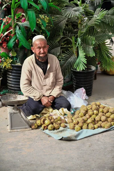 中国和田 2017年10月3日 维吾尔族土尔族的满脸胡须 头戴白色绣花头巾的老人坐在地上 在该市的集市上出售青绿的青苹果 新疆地区 — 图库照片