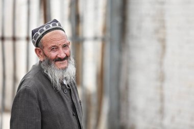 Hotan, Çin-3 Ekim 2017: Uygurlar çoğunlukla Uygur Özerk Bölgesi 'nde yaşayan bir Türk halkıdır. Uzun gri sakallı, gülümseyen yaşlı adam pazar yerinin arka tarafında yürüyor..