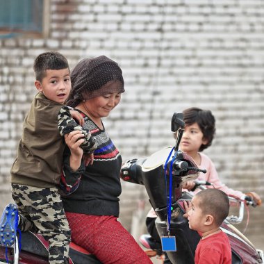Hotan, Çin-3 Ekim 2017: Uygurlar çoğunlukla Uygur Özerk Bölgesi 'nde yaşayan bir Türk halkıdır. Anne ve oğul Pazar pazarının arka tarafına park etmiş kadının scooterına binecekler..