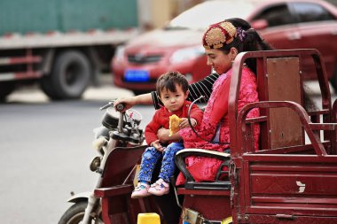 Hotan, Çin-3 Ekim 2017: Uygurlar çoğunlukla Uygur Özerk Bölgesi 'nde yaşayan bir Türk halkıdır. Bir çift çocuklu genç kadın pazar yerinin aşağısında faytona biniyor..