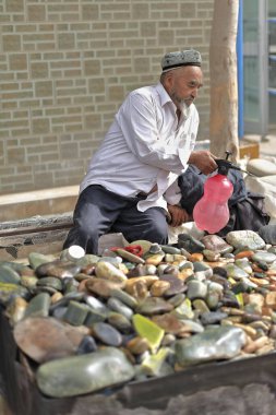 Hotan, Xinjiang, Çin-4 Ekim 2017: Yurungkax nehrinin yakınındaki Yeşim Çarşısı 'nda sattığı minerallerin üzerine Uygur tezgahındaki satıcı onları parlak ve parlak göstermek için su serpiyor..